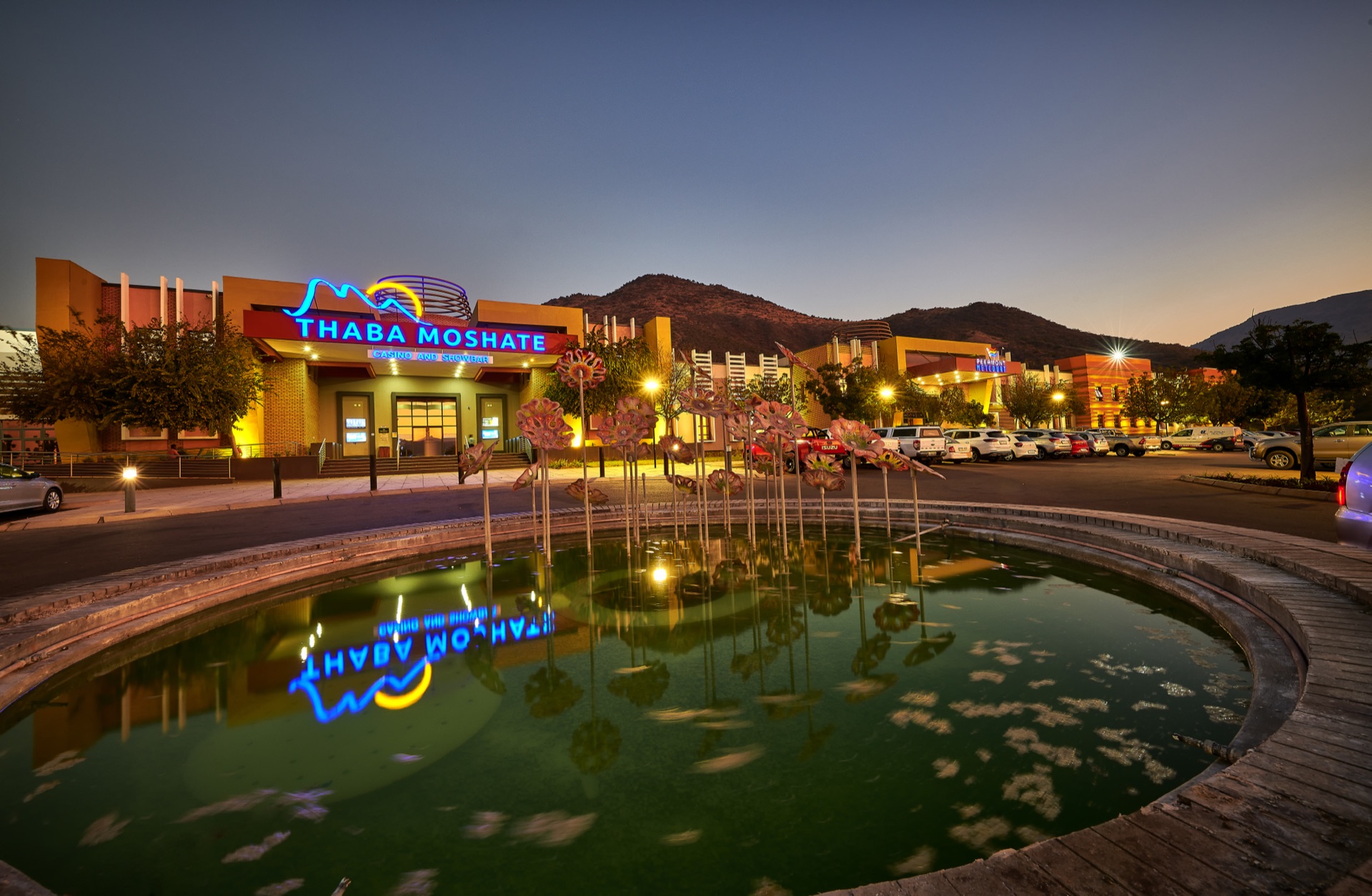 Illuminated casino entrance sign reflected in the fountain at dusk, Thaba Moshate, Burgersfort